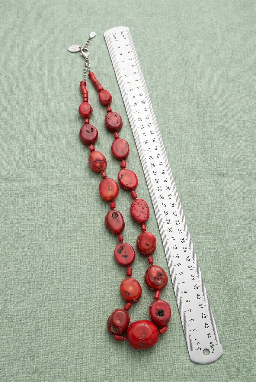 Red mottled bead necklace laid doubled beside an inch measuring tape for scale