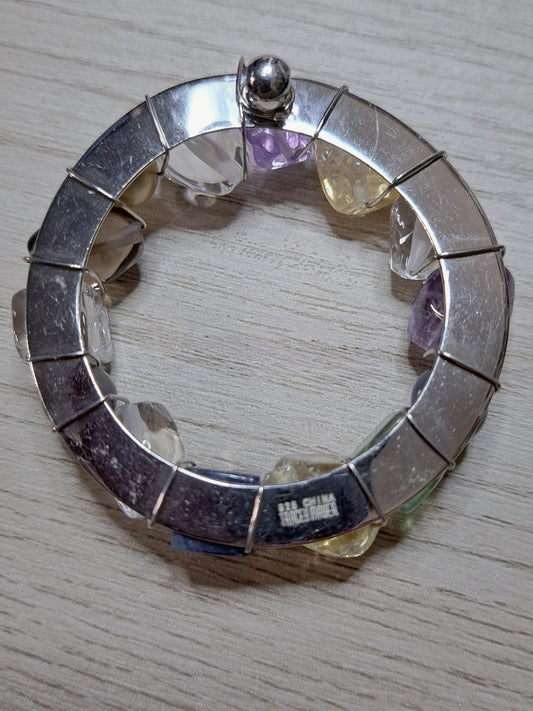 Reverse of circular jewelry piece showing silver-colored backing, wire wraps, and maker-mark area
