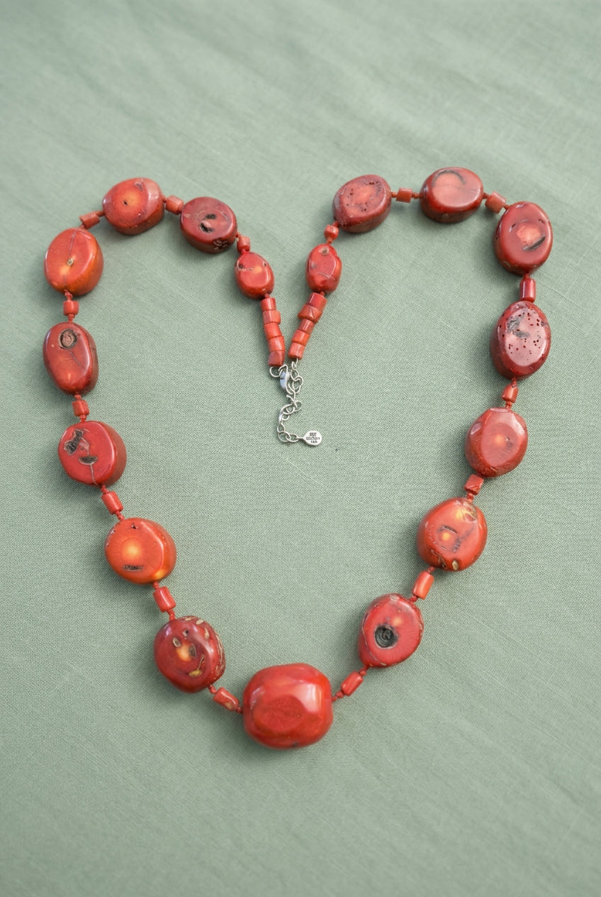 Coral-red mottled bead necklace arranged in a curved shape showing faceted center bead