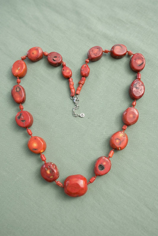 Coral-red mottled bead necklace arranged in a curved shape showing faceted center bead