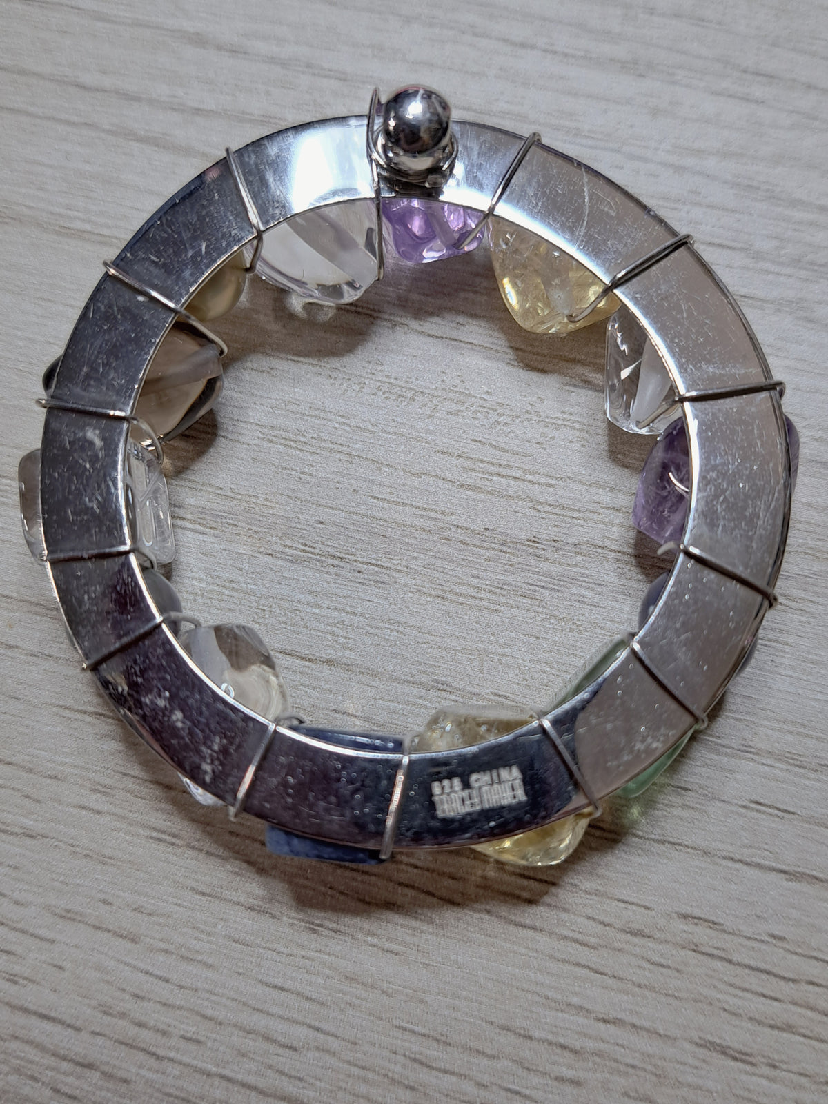 Reverse of circular jewelry piece showing silver-colored backing, wire wraps, and maker-mark area