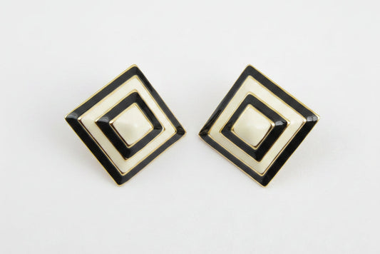 A pair of square geometric stud earrings with concentric diamond designs in cream, black, and gold, displayed on a neutral light gray background.