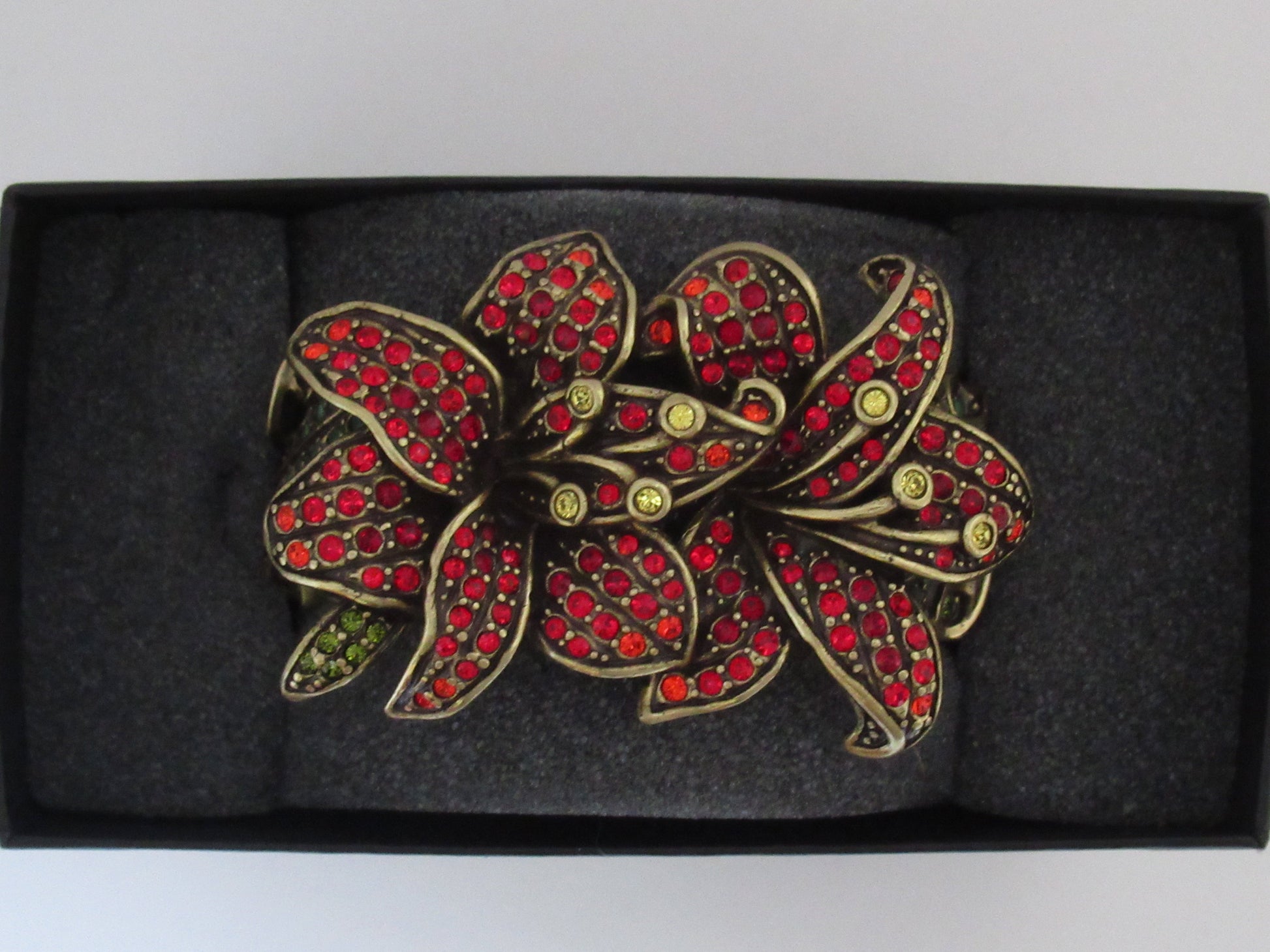 A large floral brooch featuring red rhinestones hand set in antiqued bronze metal, presented inside the original black box. 